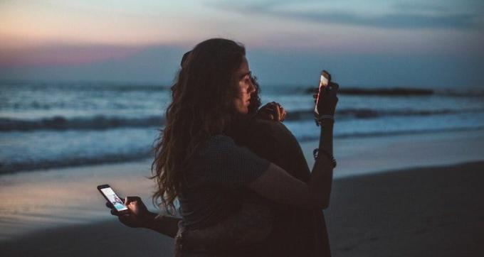 Una pareja abrazándose y mirando sus teléfonos en la playa