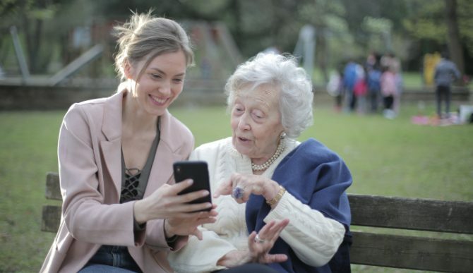 Una mujer joven y una anciana mirando un teléfono en el banco