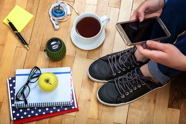 Persona con teléfono inteligente, taza de café, cuaderno, etc.